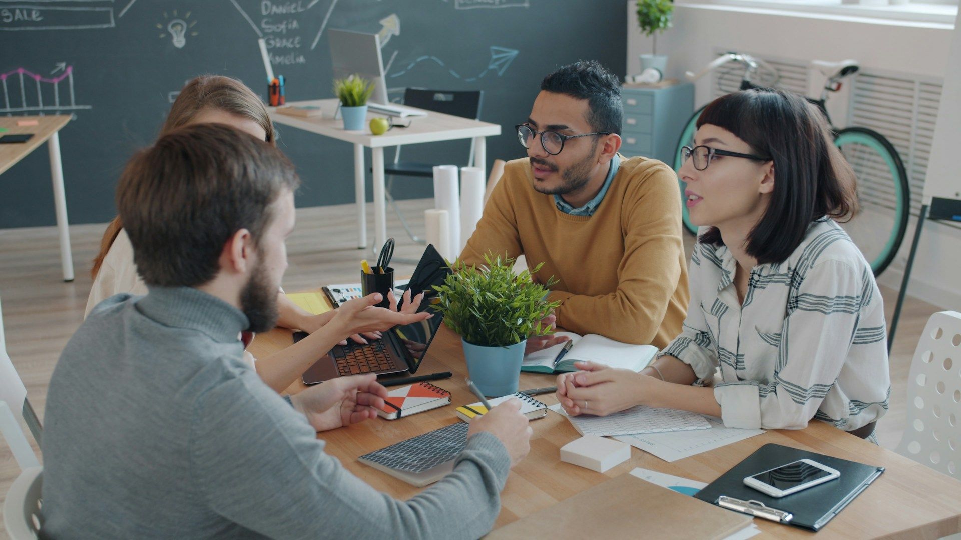 A diverse team of young professionals laughing and sharing a high-five around a table in a modern creative office